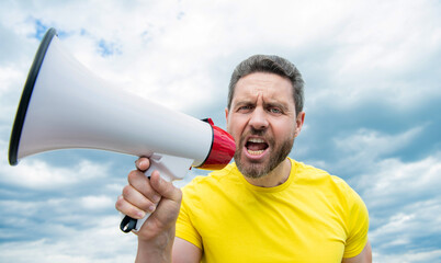 angry man in yellow shirt shout in loudspeaker on sky background