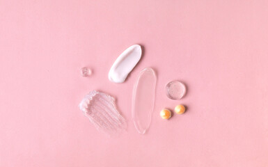 Swatches from various cosmetic products, drops of lotion, smears of creams, gels and scrubs on pink background