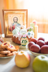Easter cake with painted eggs, apples and cookies on table in home kitchen. Church icons and candle on background. Orthodox religion theme.