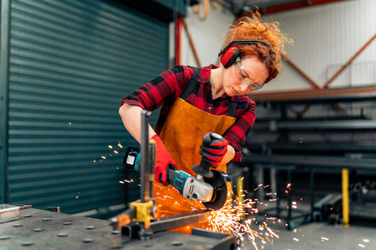 A self-employed worker is cutting a metal beam using a grinder, she is focused on her work and wearing protective gear