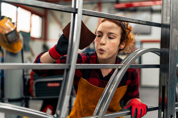 A woman sands metal bars by hand on the finished project and once again checks the quality of the...