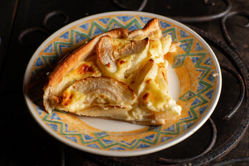 A piece of apple pie on a plate on a dark background. Sliced baked in apple dough. Charlotte.