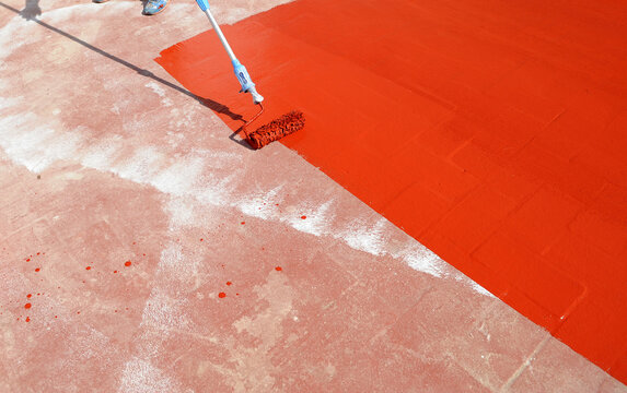 Waterproofing the roof of the building with red rubber waterproofing paint spread with a roller