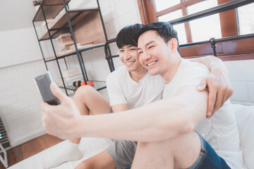 Happy Asian gay couple use mobile phone video call or selfie on bed, LGBTQ concept. Happy gay...
