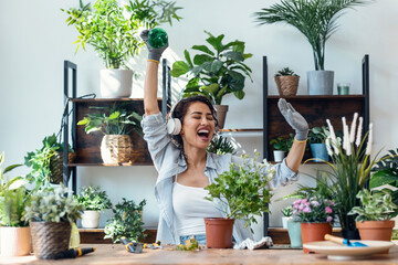 Beautiful smiling woman arranging plants and flowers while dancing in a greenhouse