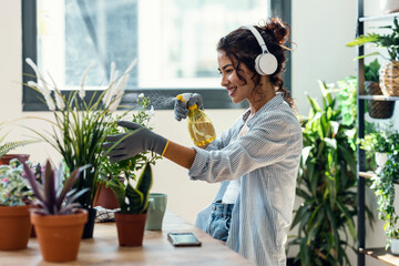 Beautiful smiling woman arranging plants and flowers while listening music in a greenhouse