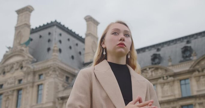 Serious Blonde Woman In Makeup Standing In Front Of Ecole du Louvre In Paris, France. low angle