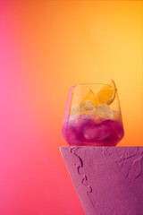 Pink champagne and butterfly pea flower cocktail with ice on a stage with gradient background. Advert concept with copy space front view.