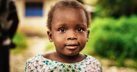 Close Up Portrait of a Cute African Little Todller Looking at the Camera with Blurred People Moving...