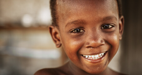 Close Up Portrait of a Shy Authentic African Boy Smiling and Laughing at the Camera with a Blurred...