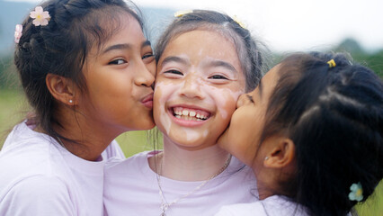 Three little cute child asia sisters kiss cheek cuddle hug look at camera smile fun having good...