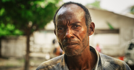 Portrait of Authentic Old African Man Looking Seriously at the Camera with Blurry Background. Senior Male with a Strong Firm Gaze Living in Rural Village, Keeping the Traditions Alive © Kitreel