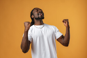 Portrait of excited african guy celebrating success with clenched fists against yellow background
