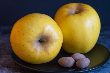 Two opal apples and three chocolate-covered almonds on a black plate.