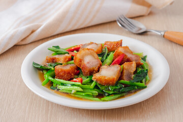 Stir fried kale with crispy pork in oyster sauce on white plate