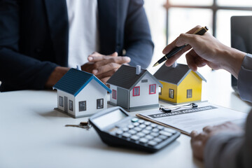 Two young Asian businessmen or architects are describing architectural house model in their office together for the construction of  housing estate project in  prime location the location is perfect