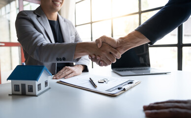 Two young Asian businessmen shake hands after signing a contract to invest in a village project. real estate, with businesswomen joining in showing joy and clapping in the office.