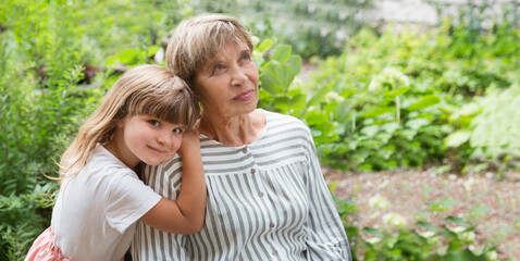 grandmother and little granddaughte hag and having fun together in the garden. Happy family enjoying summer outdoors.