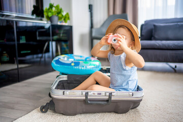 Little girl with suitcase baggage luggage and inflatable life buoy playing with toy camera and...