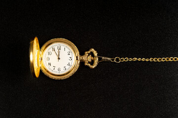 Golden pocket watch on black background showing five minutes to midnight