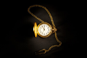 Golden pocket watch on satin background showing five minutes to midnight