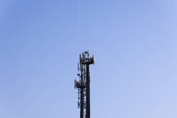 Telecommunications tower with cellular antennas and repeaters against a clear blue sky with two traces of flying aircraft