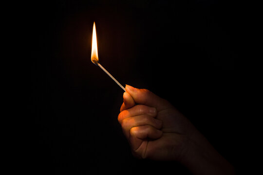 A burning match in hand. Hand with a burning match in the dark. 
