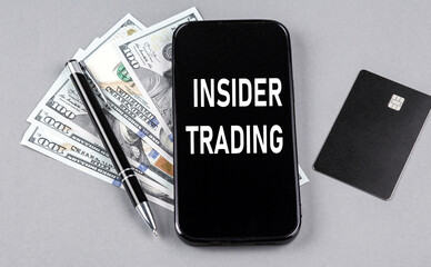 Credit card and text INSIDER TRADING on smartphone with dollars and pen. Business concept