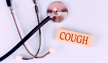 On a blue background, a stethoscope and wooden block with the word COUGH .Medical concept