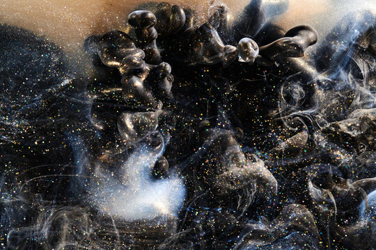 Black gold abstract ocean background. Splashes and waves of sparkling paint under water, clouds of interstellar smoke in motion