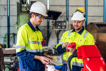 Professional two machanic engineer technician worker industrial man wearing safety uniform working control robot with heavy machine in manufacturing factory production robot line.business industry