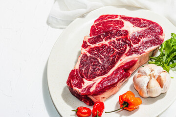 Raw Ribeye steak with spices and herbs. Dry aged meat, traditional food, hard light, dark shadow