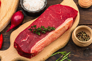 Close up of striploin steak with traditional spices and herbs. Fresh raw meat cut, wooden background