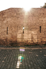 Massive old stone wall with narrow slit windows lit by warm sunlight. A fortress-like structure...