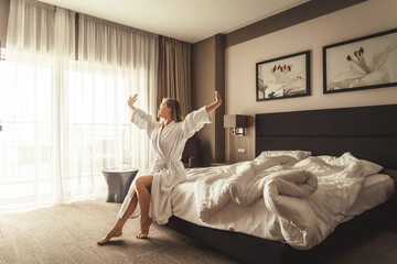 Woman in white bathrobe lying on sofa and relaxing with orange cocktail at the roof.