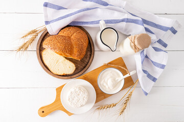 top view of the traditional products of the Jewish holiday of Shavuot. fresh bread,cottage cheese and sour cream in bowls. . wooden white background.
