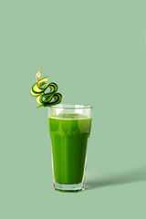 Celery juice in a glass with cucumber garnish on a green background