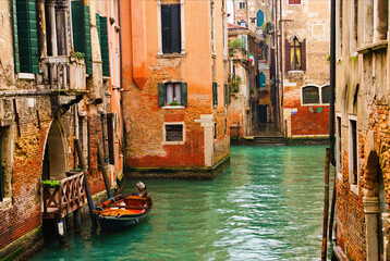 Fototapeta na wymiar Typical cityscape view of Venice. Narrow canal with emerald water between ancient red brick buildings. Famous touristic place and travel destination in Europe. Winter drizzle day in Venice