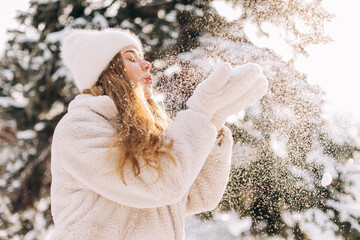 Woman dressed in a light eco-fur coat blows on the snow