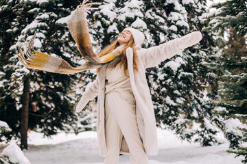 Young woman dressed in a light faux fur winter coat plays with snow in winter