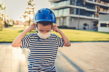 Fototapeta na wymiar New Normal. Toddler boy on bicycle wearing protective mask and helmet. A boy adjusting a mask on his face while riding a bicycle.