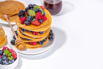 Healthy summer morning breakfast pancakes with fresh berry. Stack of traditional pancakes with blueberry, raspberries, honey. Healthy morning breakfast on white sunny background