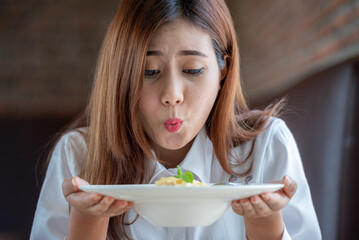 Woman in white clothes holding and smell white dish plate with pasta homemade spaghetti marinara in restaurant background. Lady smell and eat pasta spaghetti by fork.