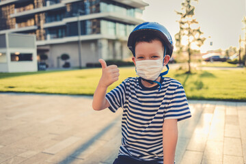 Little Caucasian boy wearing helmet and mask for protection and show thumbs up gesture for good air...