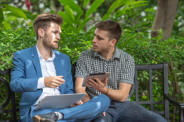 Two businessman or gay sitting at chair in park while using digital tablet and paper work plan for talk discussion team working online togetherness while consulting.