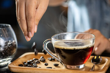 black drip coffee in glass cup, Barista making drip coffee by pouring spills hot water on coffee bean. Barista serve holding cup of hot black coffee or americano for serve on wooden table cafe shop