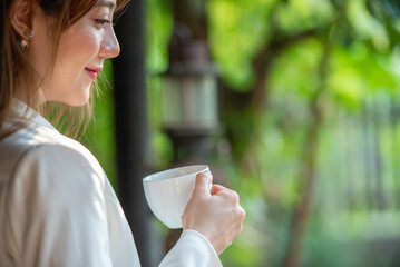 Asian woman holding hot coffee in paper mug cup to sniff smell of espresso in morning sunlight....