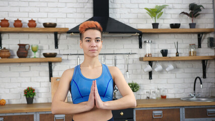 Woman with colorful haircut does yoga asana in kitchen