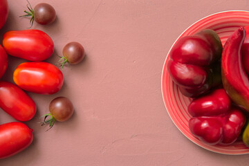 Naklejka na ściany i meble Fresh tomatoes and red peppers lying on a plate, Pink background. View from above