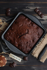 Chocolate brownie with cherries lies in a metal form, which stands on a wooden background.
